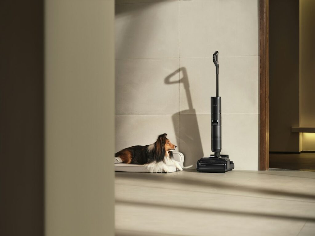 A dog rests near a vacuum cleaner on the floor